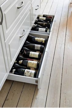 an open drawer in the middle of a kitchen filled with bottles of wine on top of wooden flooring