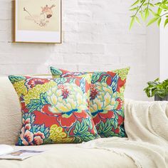 two pillows sitting on top of a white couch next to a potted green plant