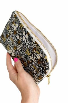 a hand holding a black and white flowered pouch with gold zippers on it