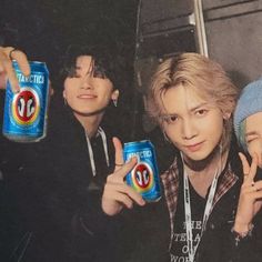 three young men are holding up two cans of soda and one is pointing at the camera