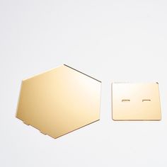 two pieces of gold metal sitting next to each other on a white surface with one piece missing