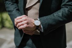 a man wearing a suit and holding his hand on his wrist while standing in the street