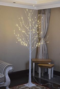 a white lighted tree in a living room next to a chair and table with a rug on the floor