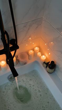 a bathtub filled with candles and soap next to a wall mounted faucet