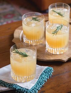 three glasses filled with lemonade sitting on top of a wooden table next to a blue and white towel