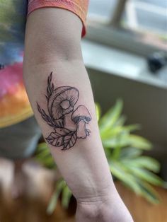 a woman's arm with a mushroom and leaves tattoo on the left inner forearm