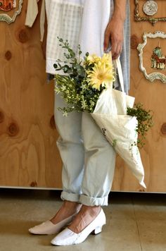 a woman standing in front of a wooden wall holding a bouquet of flowers and a white bag