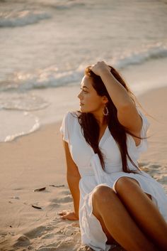 a woman is sitting on the beach with her head in her hands and looking off into the distance