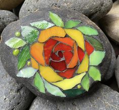 a rock with a stained glass rose on it sitting next to some rocks and leaves