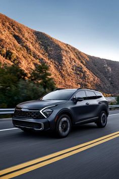 the front end of a gray suv driving down a road with mountains in the background