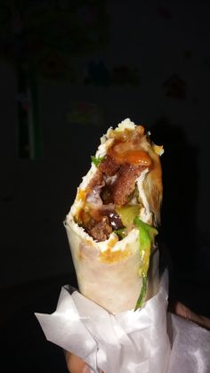 a person holding up a burrito wrapped in wax paper with toppings on it