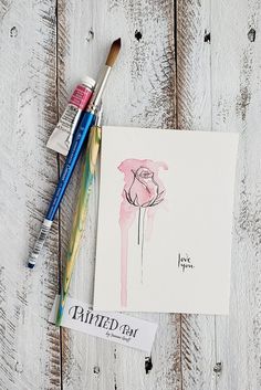 some paint brushes are next to a card with an image of a flower on it