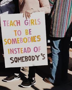 two people holding a sign that says teach girls to be somebody instead of somebody's