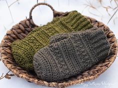 two knitted hats sit in a basket on the snow covered ground, one is green and the other is brown