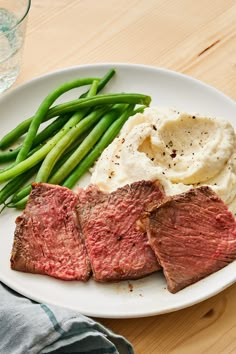 steak, mashed potatoes and green beans on a white plate with a glass of water