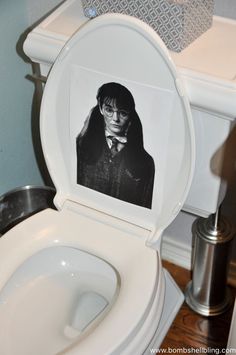 a toilet with a photo of harry potter on the lid and in front of it is a silver trash can