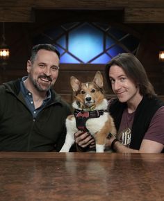 two people sitting at a table with a dog in their lap and one person holding the dog