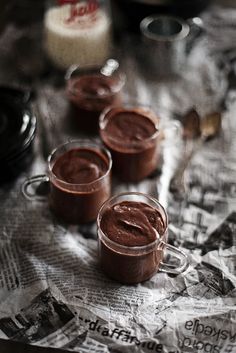 three cups filled with chocolate pudding sitting on top of a newspaper