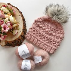 two balls of yarn and a knitted hat on top of a piece of wood