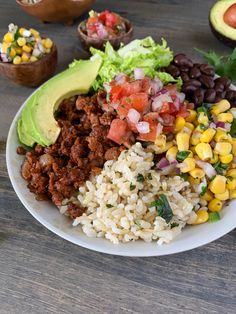 a white plate topped with rice, beans and veggies next to avocado