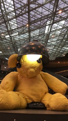 a large yellow teddy bear sitting on top of a wooden shelf under a glass ceiling