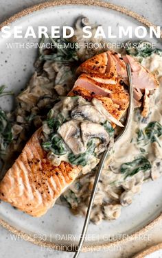 a white plate topped with salmon and spinach covered in gravy next to a fork