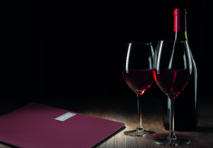 two glasses of wine next to a bottle of wine on a wooden table in the dark