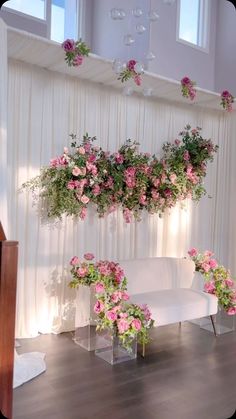 a white couch sitting in front of a window filled with pink flowers and greenery