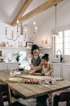 a woman and two children are in the kitchen preparing food on a wooden table with an apron