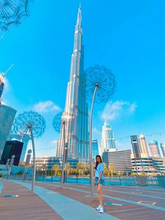 a woman standing in front of the burj building, with ferris wheel sculptures behind her