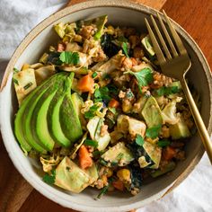 a bowl filled with vegetables and avocado next to a fork