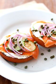 two pieces of bread with salmon and capers on it sitting on a white plate