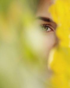 a woman's eyes are seen through the yellow flowers on her face and behind her is a blurry image of herself