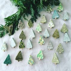 small wooden christmas trees are arranged on a white surface next to some green leaves and branches