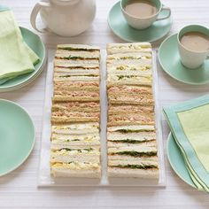 there are many sandwiches on the table with cups and saucers next to each other