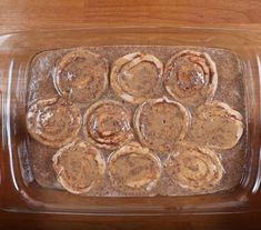 a glass dish filled with cinnamon rolls on top of a wooden table next to a knife