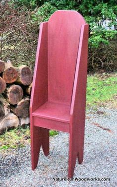 a red wooden chair sitting next to a pile of logs in front of some bushes