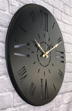 a black clock mounted to the side of a white brick wall with roman numerals