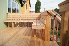 a wooden bench sitting on top of a wooden deck next to a green wall and yellow house