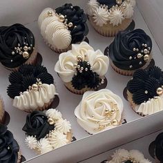 cupcakes decorated with black, white and gold icing in a cardboard box