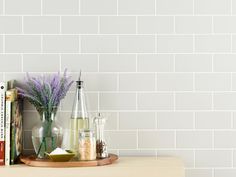 a shelf with books and vases on it in front of a white brick wall