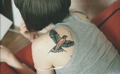 a woman with a bird tattoo on her arm and shoulder, looking down at the ground