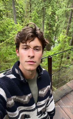 a young man standing on a bridge in the woods