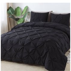 a bed with black comforter and pillows on it next to a potted plant