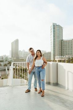 a man and woman standing on top of a roof next to each other in front of tall buildings