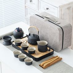 a tray with cups and teapots on it next to a suitcase filled with other items