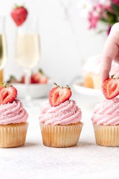 two cupcakes with pink frosting and strawberries on top are being held by a hand