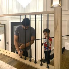 a man standing next to a little boy on top of a wooden floor in front of a window