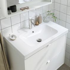 a white bathroom sink sitting next to a mirror on a wall above a shelf with a potted plant in it