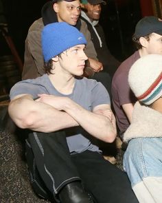 four young men sitting on the ground with one wearing a blue hat and another in grey shirt